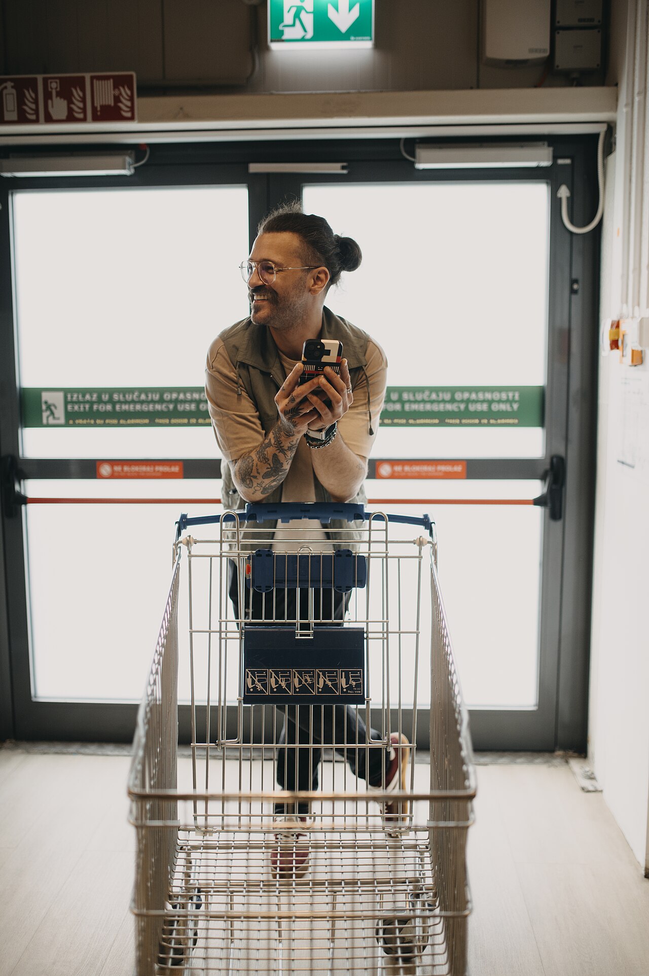 Man holding a smartphone while pushing a shopping cart in a grocery store during daytime.jpg